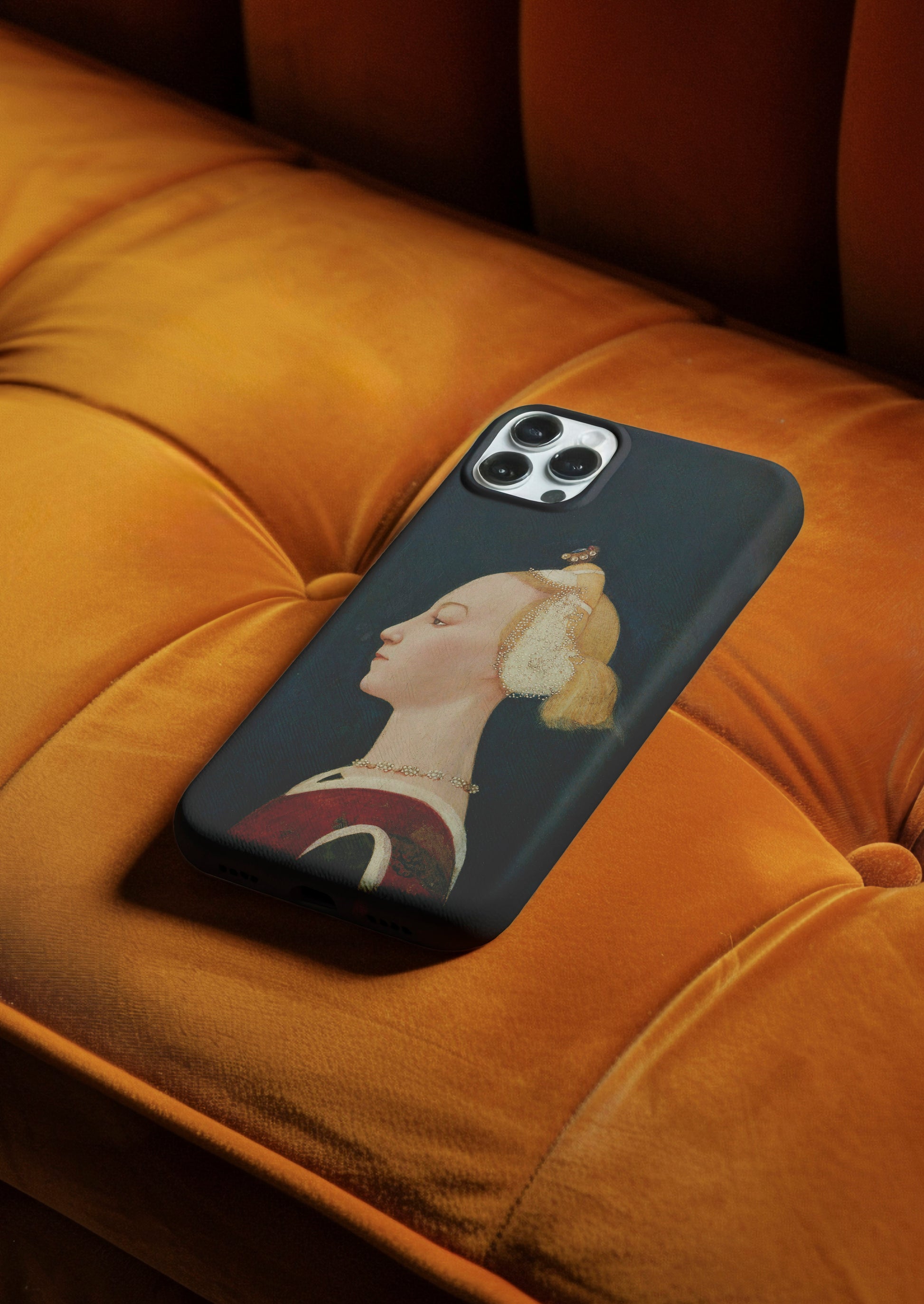 A close-up shot of the ART SNOB "Master of the Castello Nativity Portrait of a Woman" phone case lying on a luxurious, gold-coloured velvet couch. The image highlights the detailed print of the classical Renaissance painting on the durable phone case, showcasing its stylish and protective design.