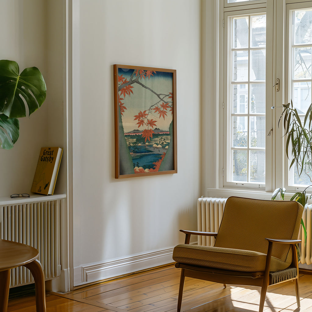 A framed art print depicting a Japanese-style coastal landscape with red maple leaves hangs on a white wall in a sunlit room with a wooden chair, window, and plants.