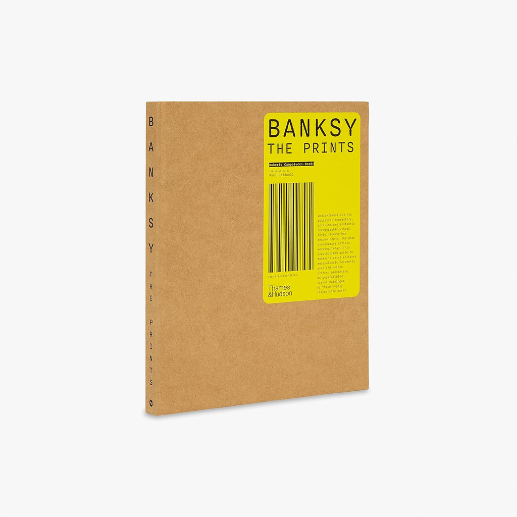 Three quarter view of Banksy The Prints coffee table book showing spine and front cover with kraft paper design and yellow label published by Thames and Hudson