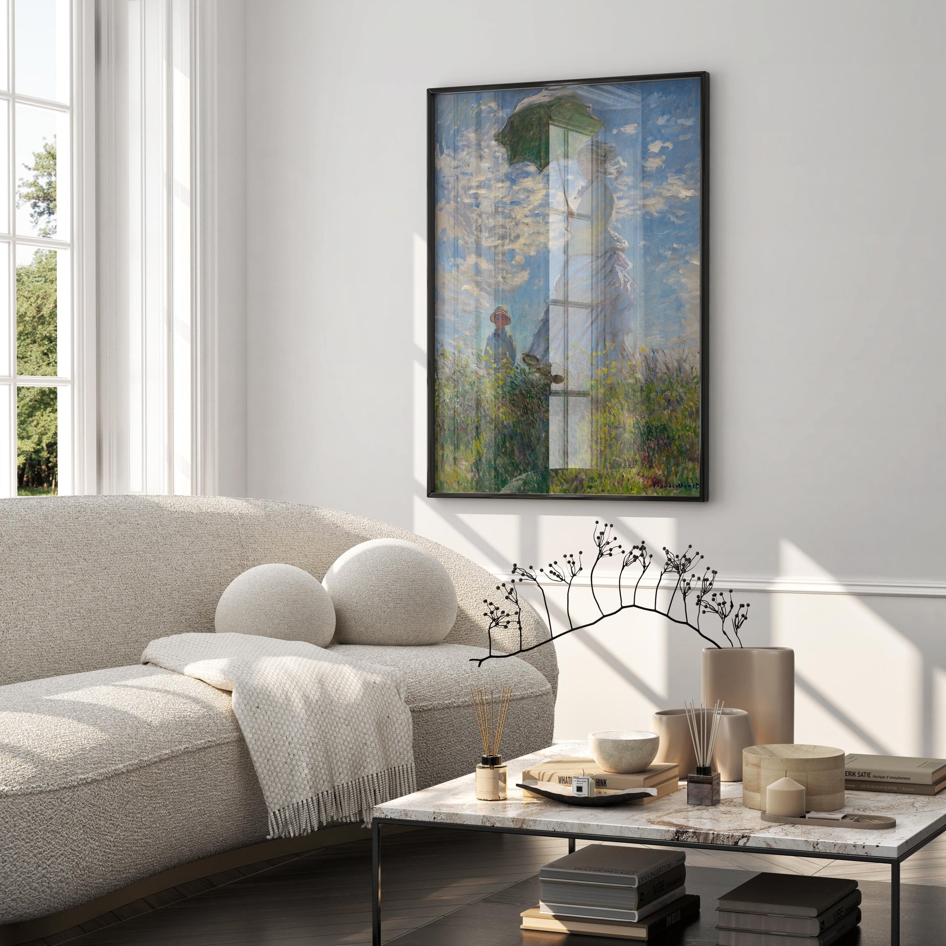 A large, black-framed art print of Claude Monet's Impressionist masterpiece, "Woman with a Parasol," hanging on a white wall above a beige sofa. This wall art piece serves as a focal point in a modern, elegant living room and is an excellent example of classic art for home decor.