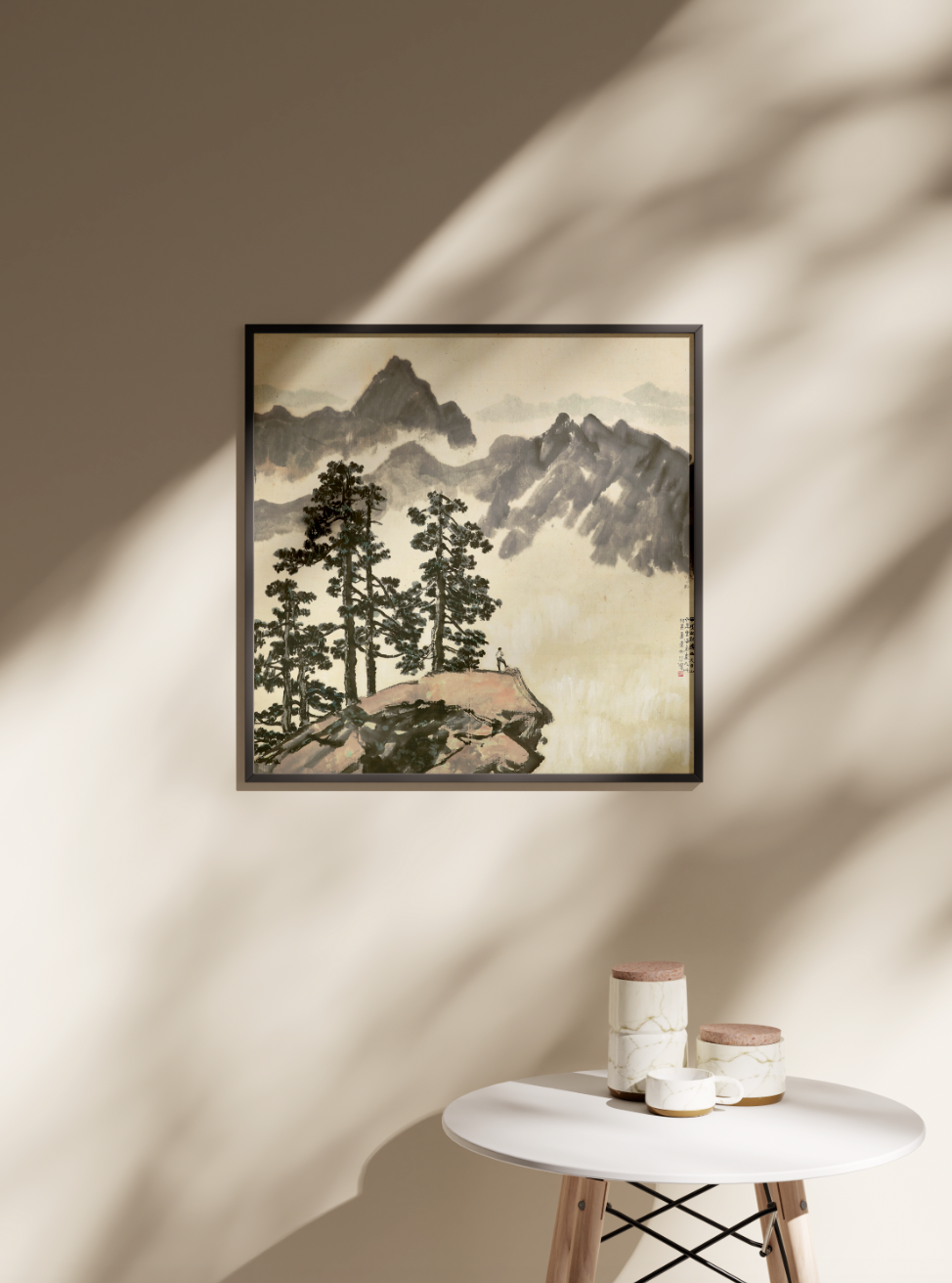 A framed Xu Beihong "Tianmu Mountains" fine art print hanging on a beige wall, with natural light and shadow from a window creating a tranquil atmosphere in a modern living room setting. The wall art is displayed above a small white side table with decorative ceramic jars, highlighting a stylish and serene home decor aesthetic.