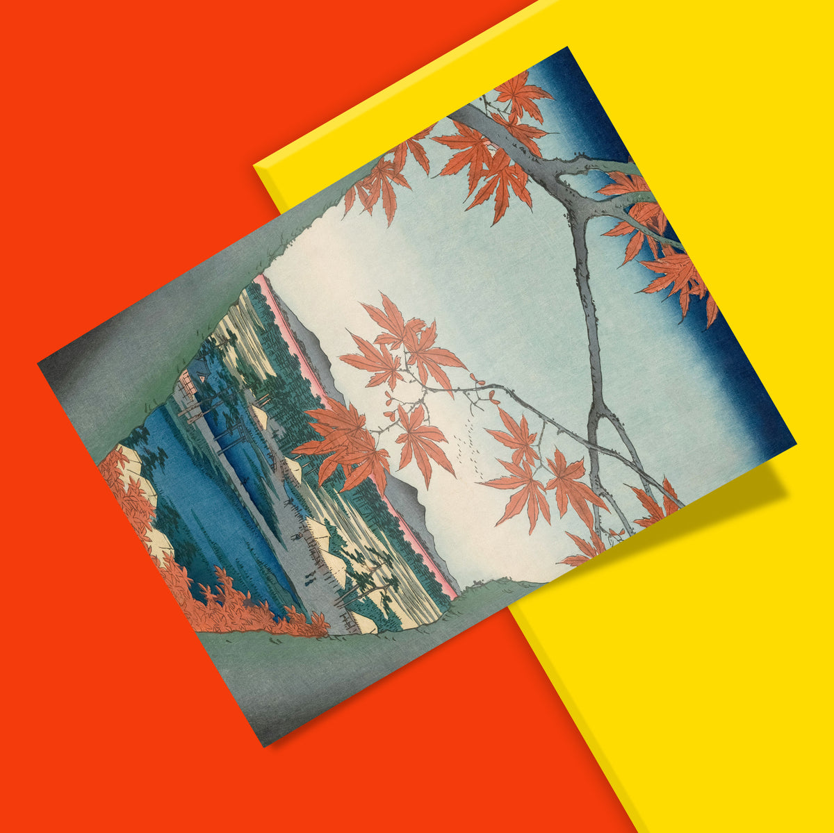 A square art print featuring a Japanese-style landscape print with red maple leaves, blue water, and mountains, styled diagonally over a bright yellow card on a solid red background.