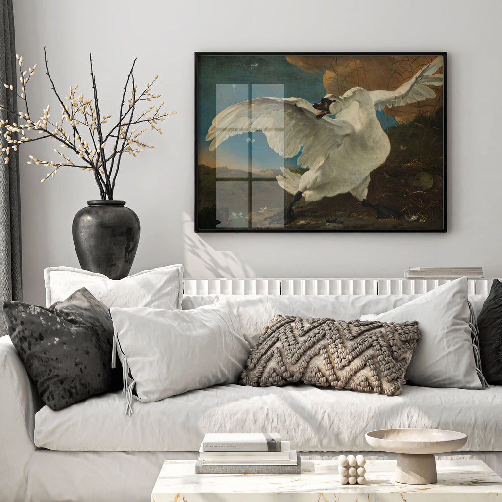 A framed art print depicting a white swan in flight, displayed on a light gray wall above a white sofa with decorative pillows in a modern living room setting.