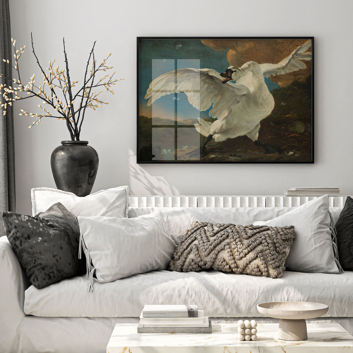 A framed art print depicting a white swan in flight, displayed on a light gray wall above a white sofa with decorative pillows in a modern living room setting.