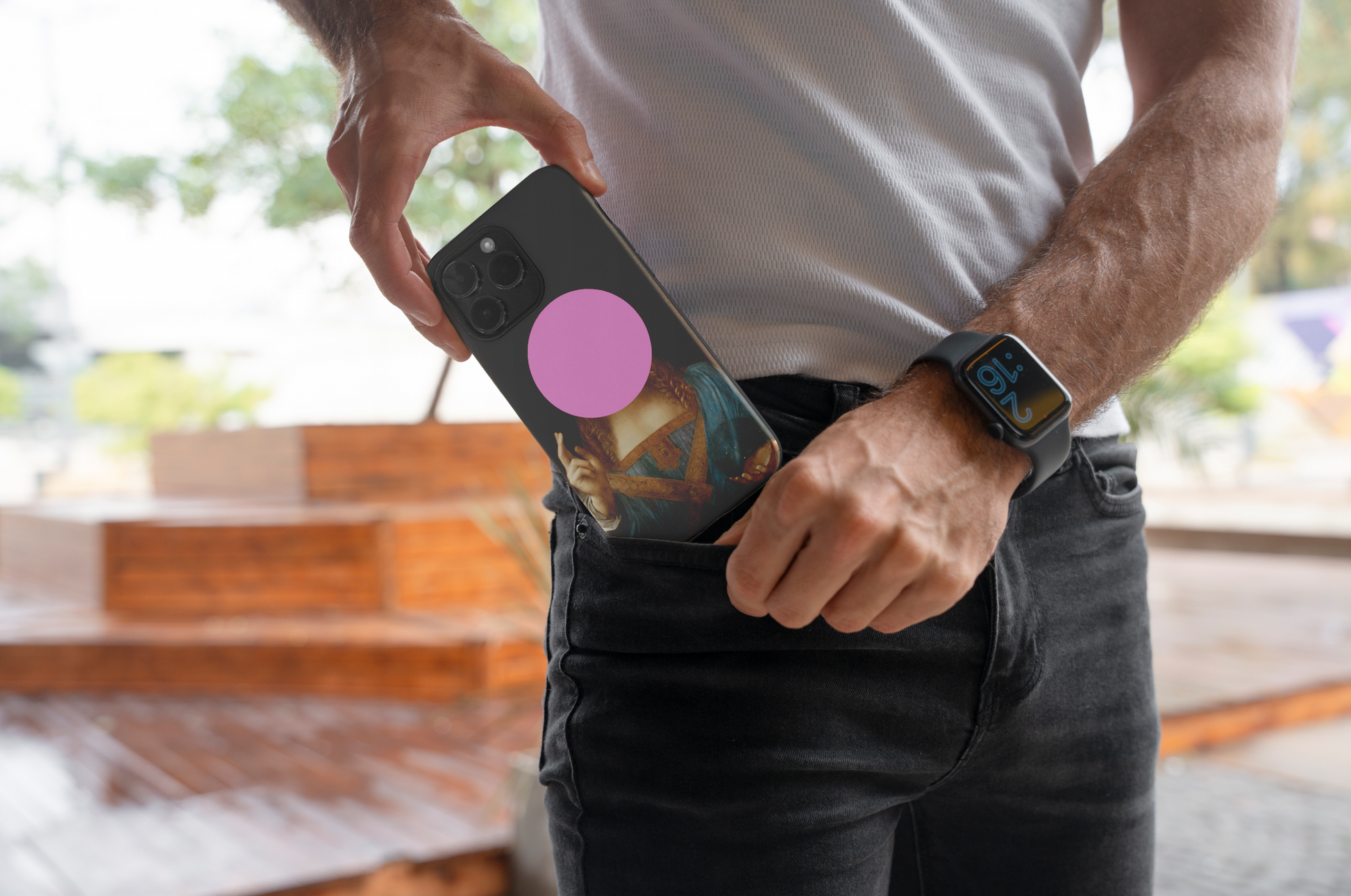 A man with a smartwatch on his wrist placing a black phone case featuring a print of Leonardo da Vinci's Salvator Mundi with a pink circle over the face, into the pocket of his black jeans. The image highlights the stylish and practical use of the ARTSNOB fine art phone case.