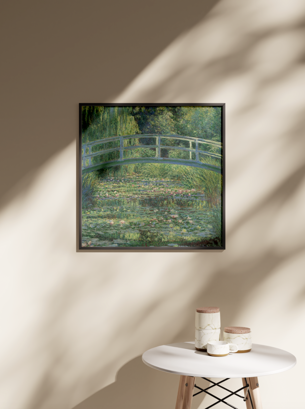 A framed art print of Claude Monet's The Water-Lily Pond hangs on a beige wall, with a dappled shadow pattern from a nearby plant, showing how the piece works as stylish wall art for a modern living space.
