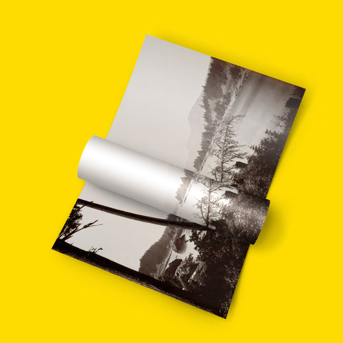 A rolled-out black and white landscape photograph print displayed on a bright yellow background.