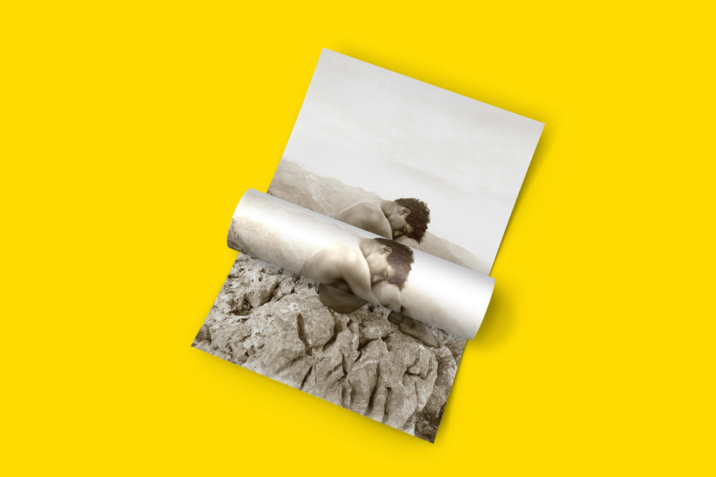 High-quality wall art of the Wilhelm von Gloeden photograph "Cain," featuring a nude man seated on rocks, embodying solitude and introspection with a timeless, sepia aesthetic.