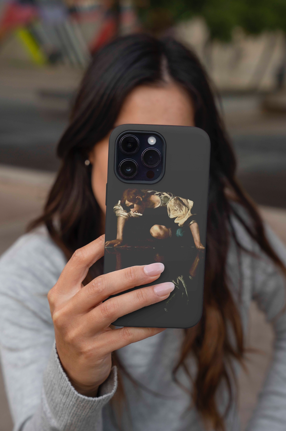 A woman holds up an iPhone with a Caravaggio Narcissus fine art phone case, showcasing the detailed painting and sleek black design.