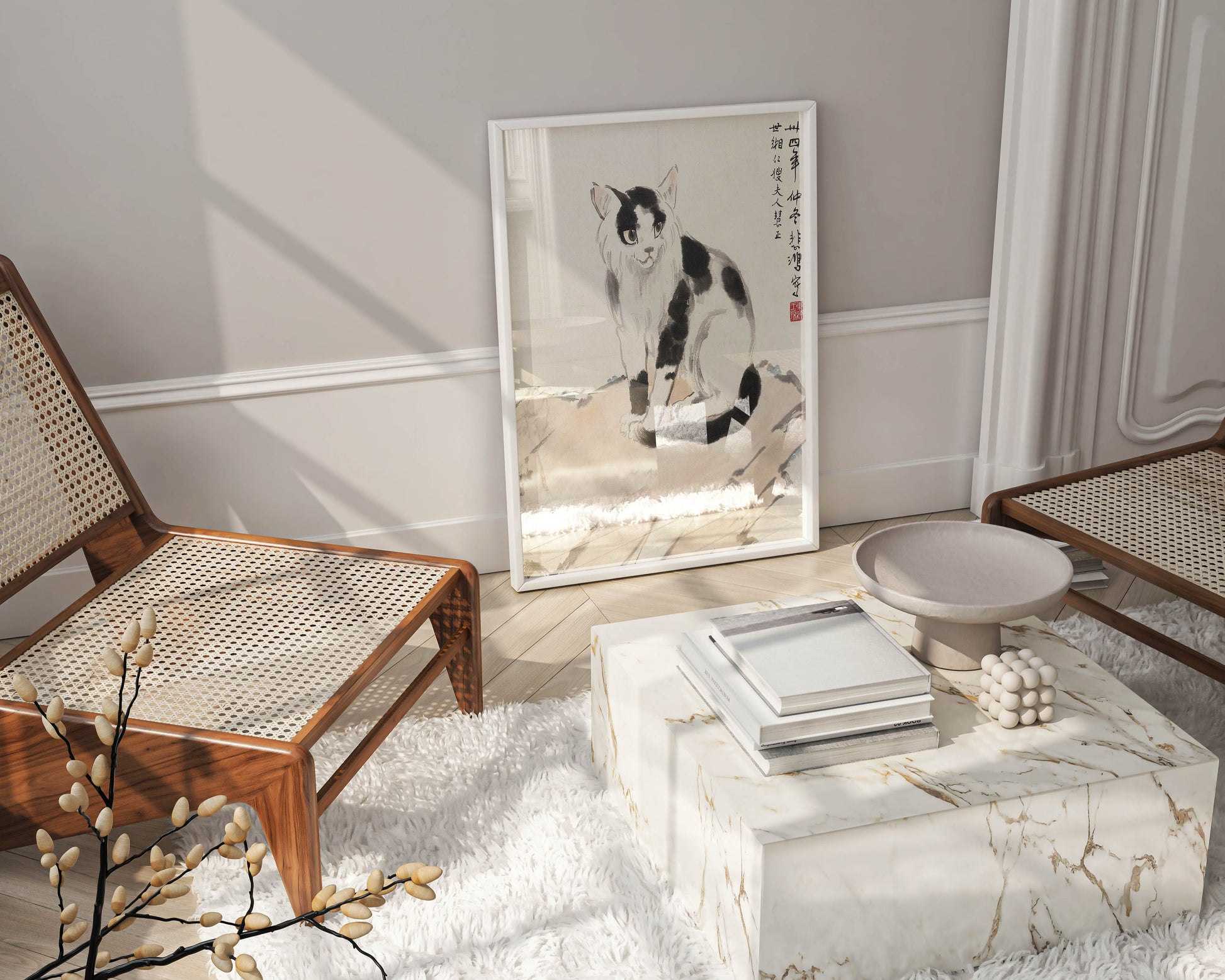 A framed art print of Xu Beihong's cat painting leaning against a wall in a room with neutral and beige home decor, including a white furry rug and wooden chairs.
